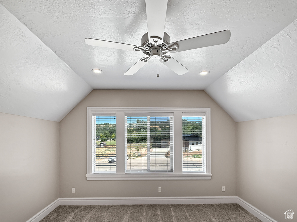 Bonus room featuring a textured ceiling, lofted ceiling, carpet, and a ceiling fan