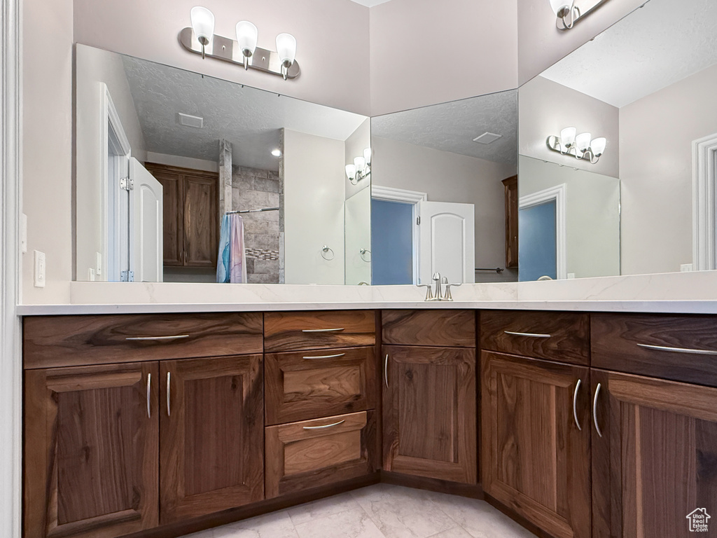 Full bathroom featuring double vanity, tiled shower, and marble look tiles
