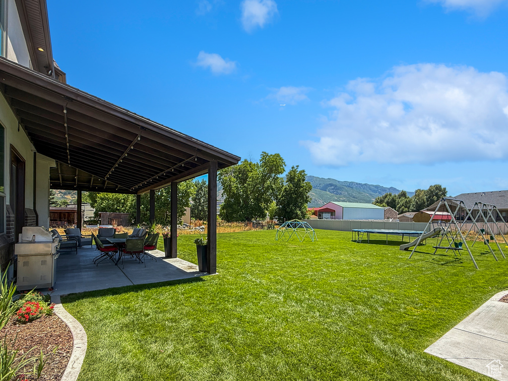 Fenced backyard featuring a playground, a patio, a trampoline, and a mountain view