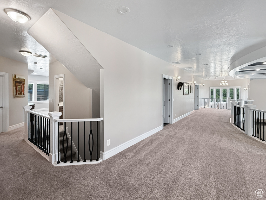 Hallway featuring an upstairs landing, carpet, a textured ceiling, and a chandelier