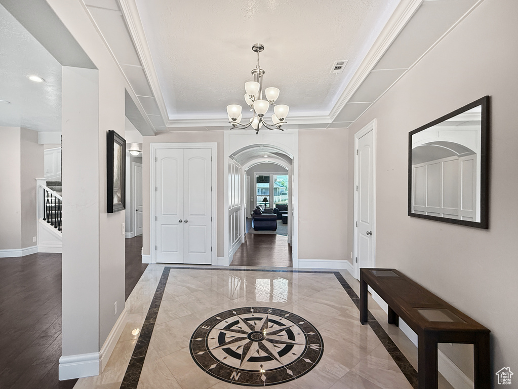 Foyer with arched walkways, a chandelier, a tray ceiling, inlaid floor details, and recessed lighting