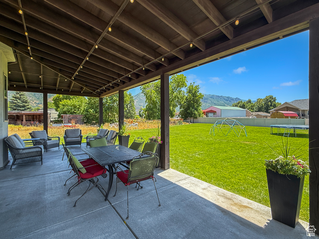 Fenced backyard with a trampoline, a patio area, outdoor dining area, a playground, and a mountain view