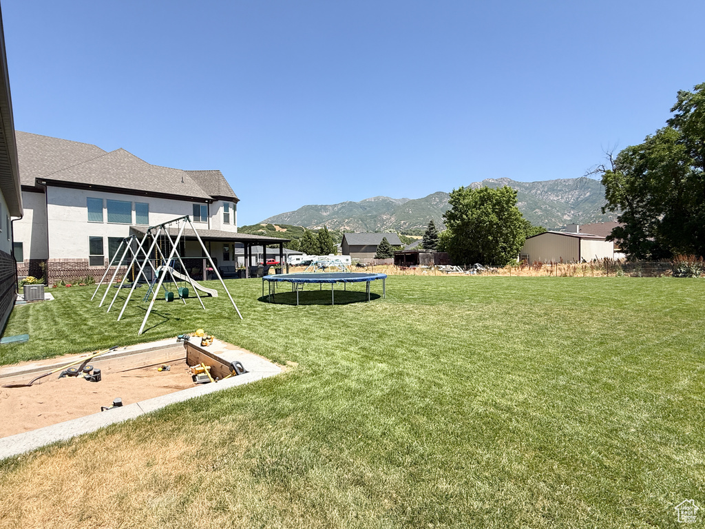 View of grassy yard with a trampoline, a playground, and a mountain view