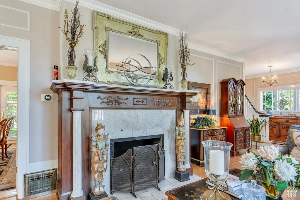Living room with ornamental molding, a tiled fireplace, a chandelier, and tile patterned flooring