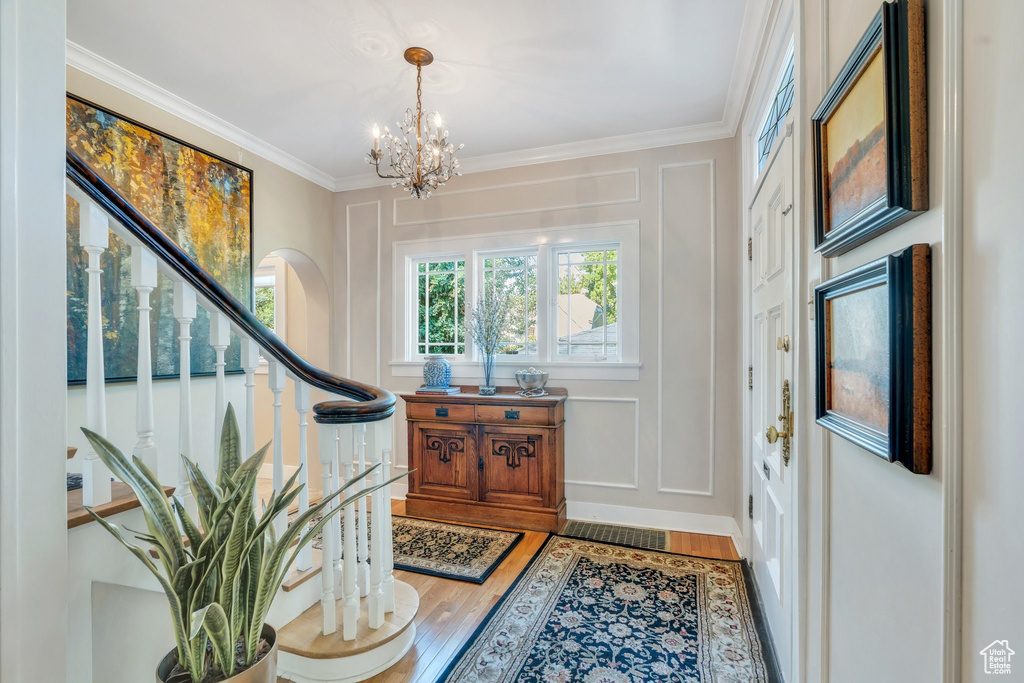 Foyer entrance featuring stairway, a chandelier, light wood-style flooring, and crown molding