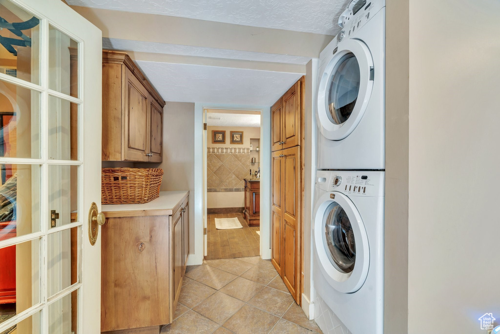 Laundry area featuring stacked washer and clothes dryer, cabinet space, and light tile patterned floors