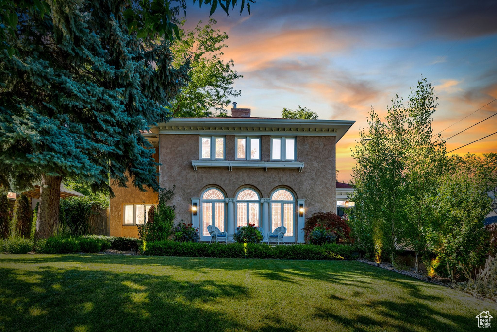 Italianate-style house featuring a chimney, a front lawn, and stucco siding