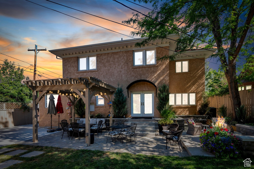 Rear view of house featuring french doors, a pergola, stucco siding, a patio area, and an outdoor living space