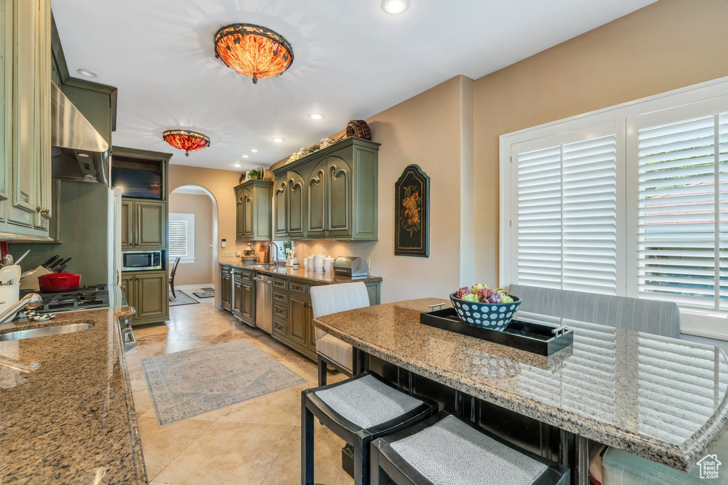 Kitchen featuring stainless steel appliances, arched walkways, green cabinets, ventilation hood, and recessed lighting