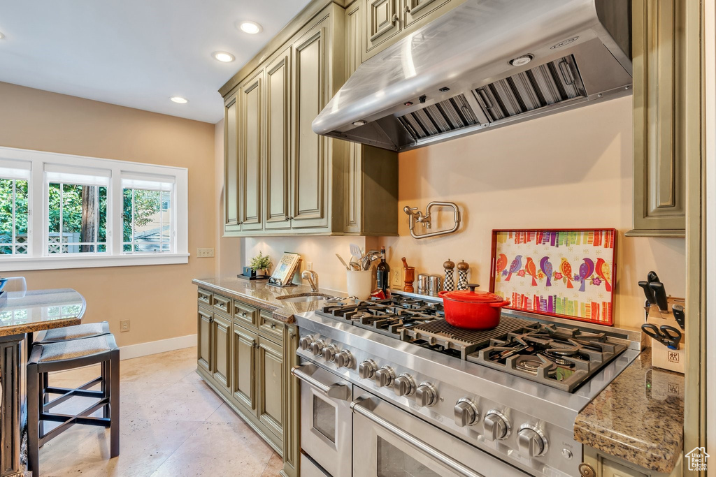 Kitchen featuring under cabinet range hood, range with two ovens, cream cabinetry, light stone countertops, and recessed lighting
