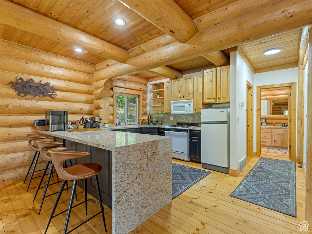 Kitchen featuring white appliances, light wood-style flooring, a kitchen breakfast bar, a wooden ceiling with exposed beams, and light stone counters