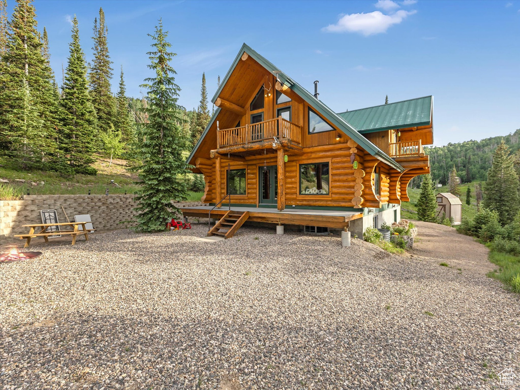 View of front of home featuring log siding, a balcony, a view of trees, a deck, and board and batten siding