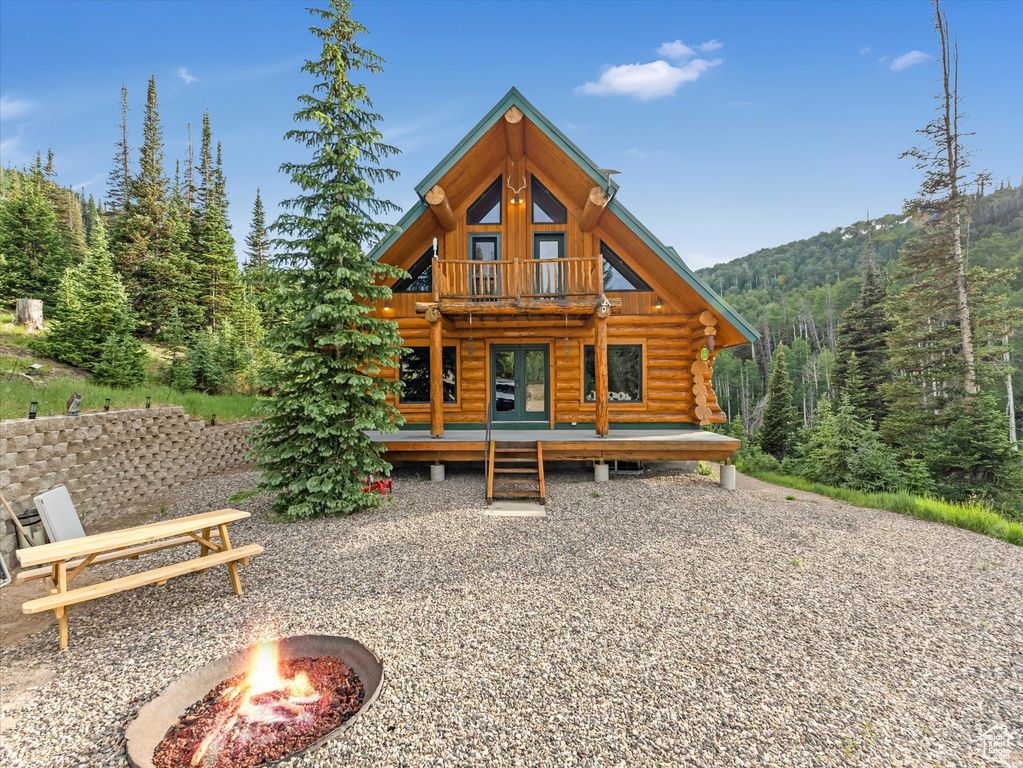 Back of house featuring an outdoor fire pit, log exterior, a view of trees, a balcony, and a deck