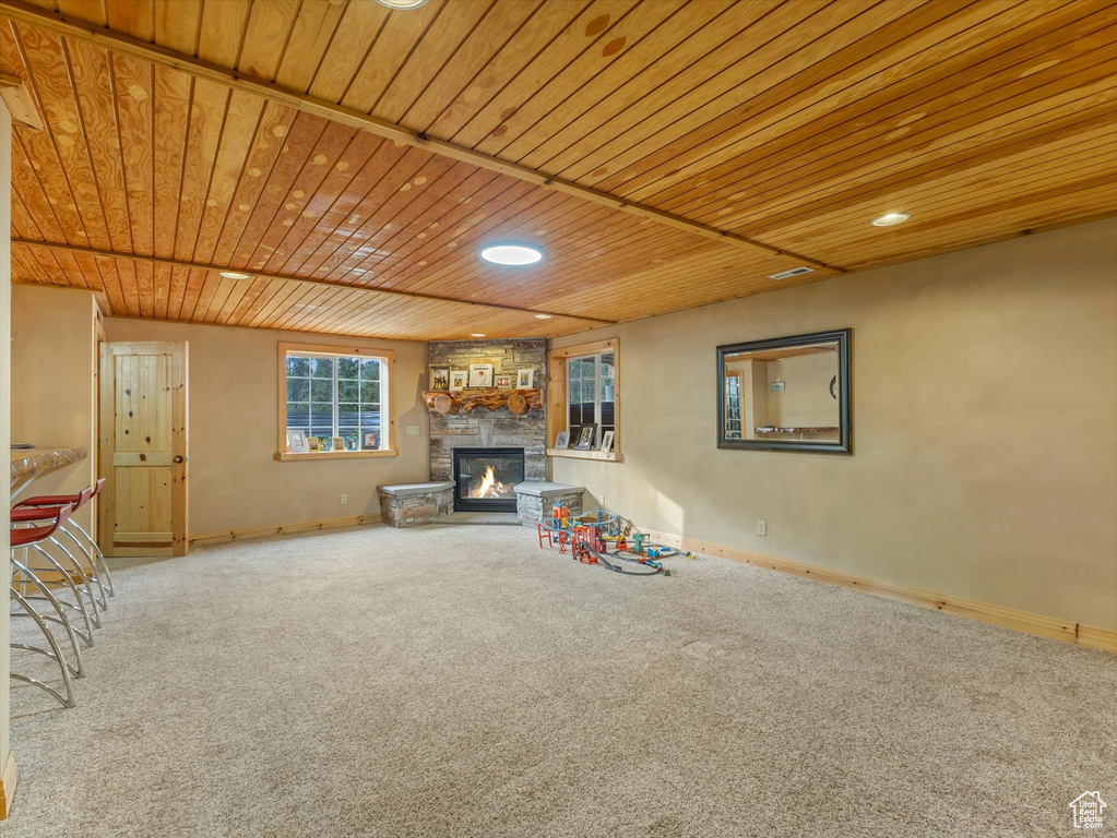 Unfurnished living room with carpet flooring, a stone fireplace, wood ceiling, and recessed lighting