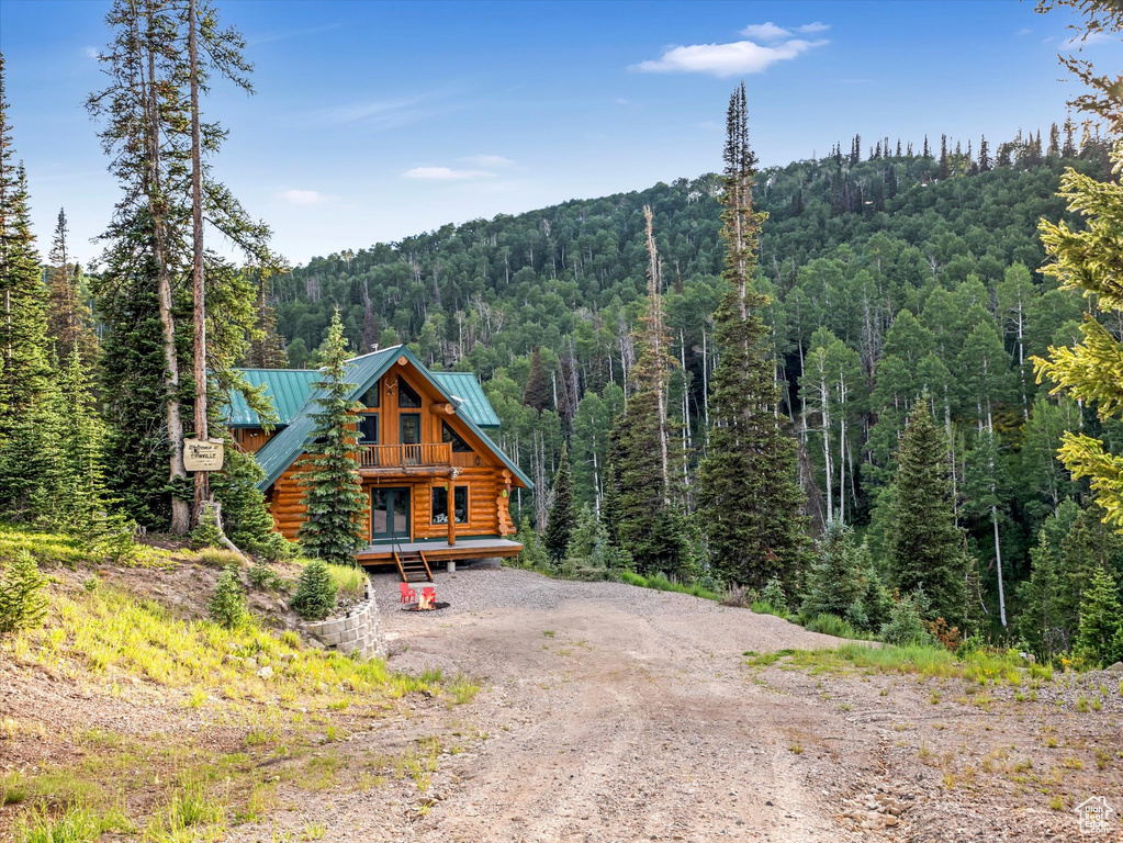 Cabin with a wooded view, log siding, a metal roof, a standing seam roof, and dirt driveway