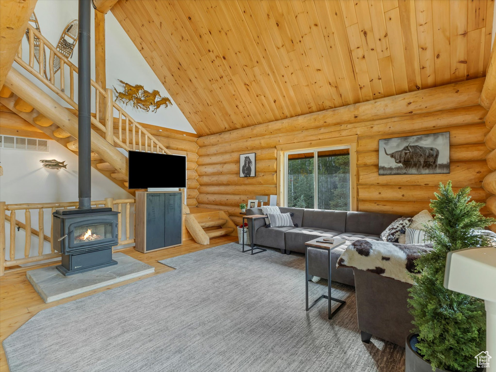 Living area featuring high vaulted ceiling, a wood stove, log walls, wooden ceiling, and stairs