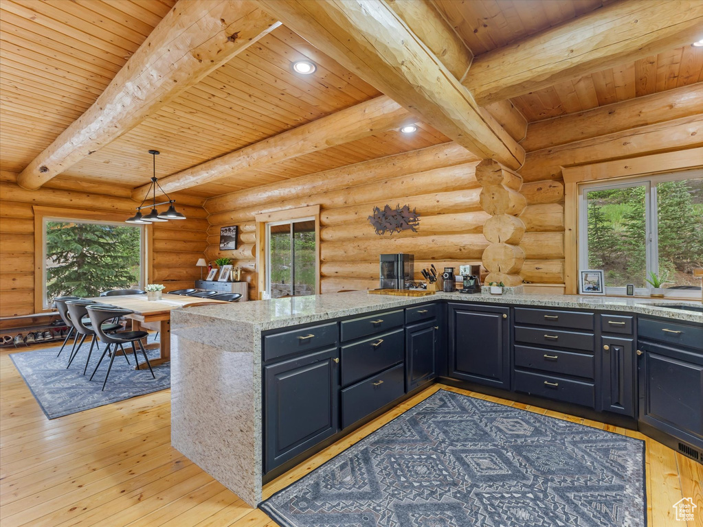 Kitchen featuring a wooden ceiling with exposed beams, light wood-type flooring, light stone counters, decorative light fixtures, and log walls