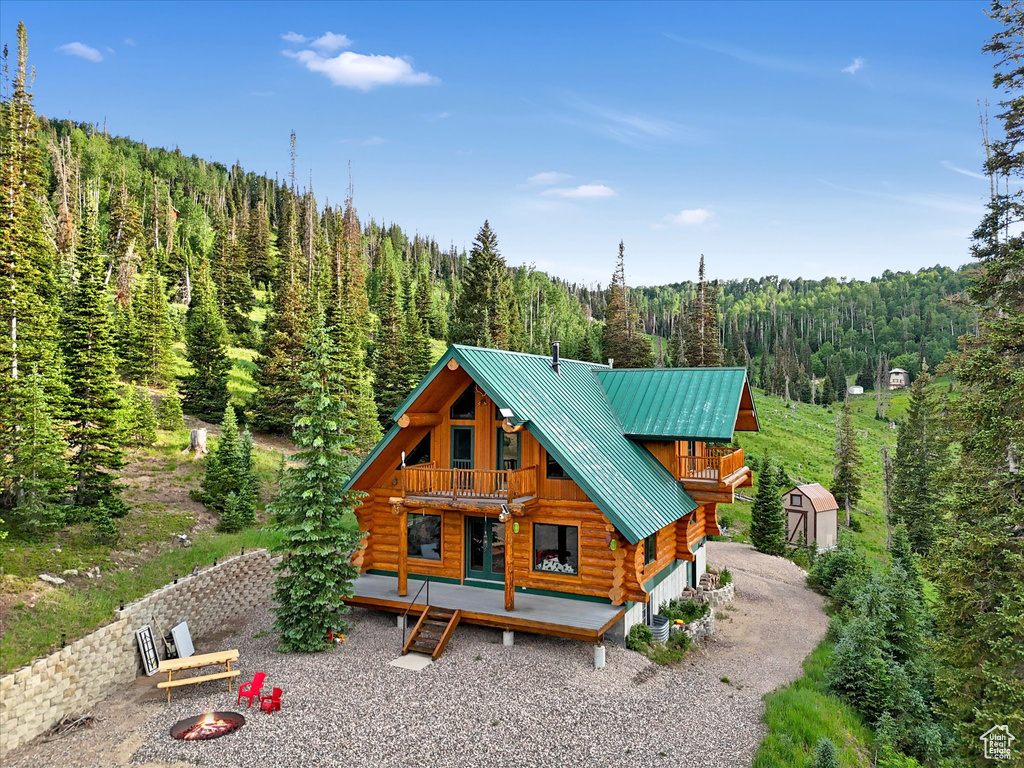 View of front of home with a forest view, log exterior, a fire pit, a metal roof, and a wooden deck