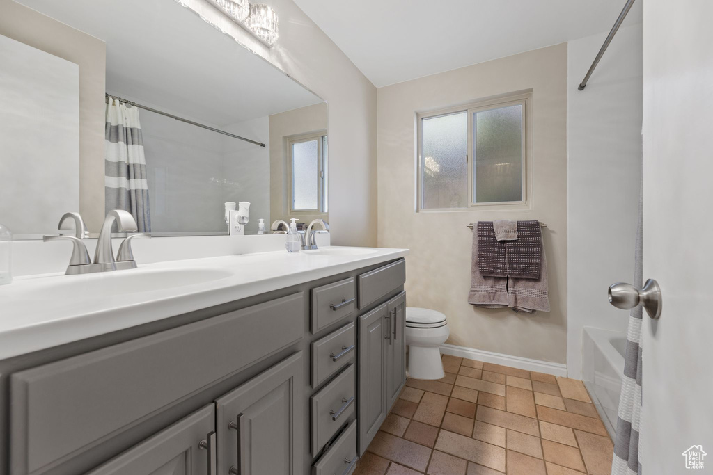 Bathroom featuring double vanity, shower / bath combo with shower curtain, and stone finish floors
