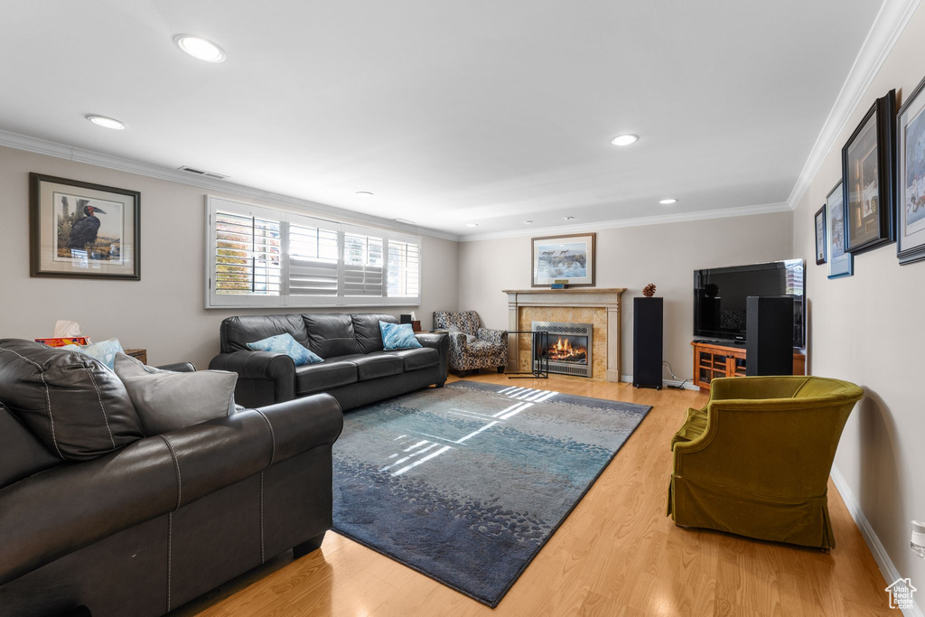 Living room with light wood-style floors, a tile fireplace, crown molding, and recessed lighting