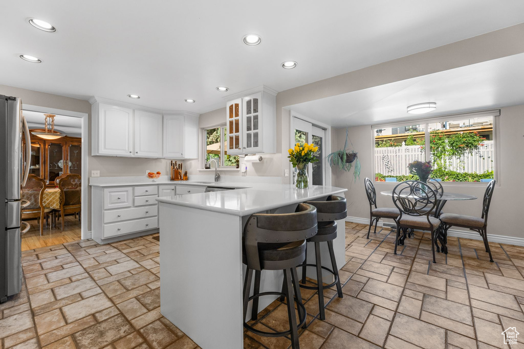 Kitchen with freestanding refrigerator, recessed lighting, a kitchen bar, a peninsula, and glass insert cabinets