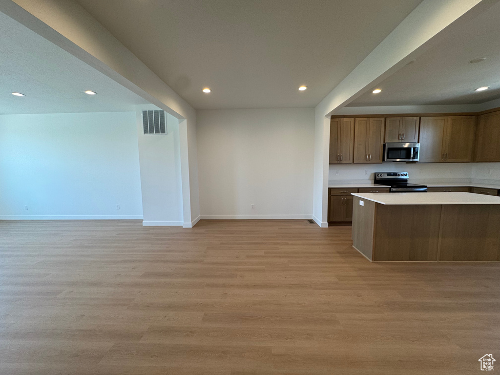 Kitchen with stainless steel appliances, recessed lighting, light countertops, open floor plan, and light wood-style floors