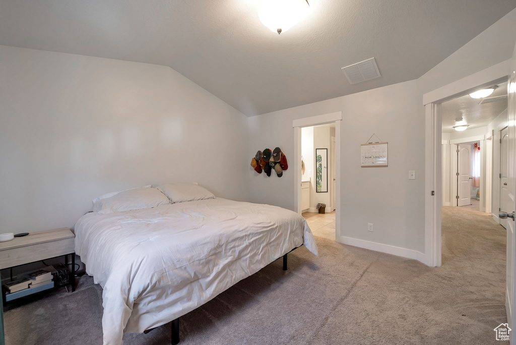 Bedroom with lofted ceiling, light colored carpet, and ensuite bath