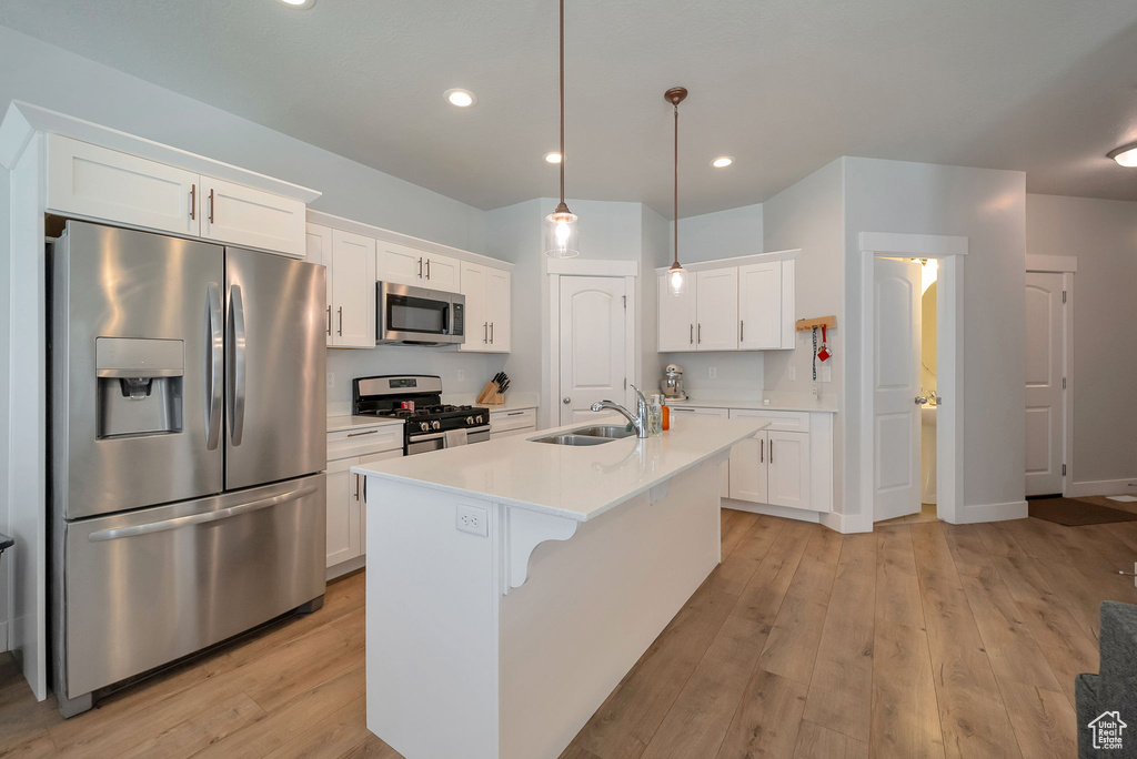 Kitchen featuring appliances with stainless steel finishes, light wood-style flooring, white cabinets, light countertops, and a kitchen island with sink