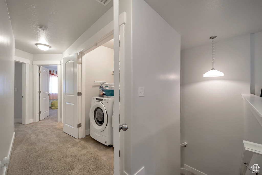 Laundry room featuring washer / clothes dryer, light colored carpet, and a textured ceiling