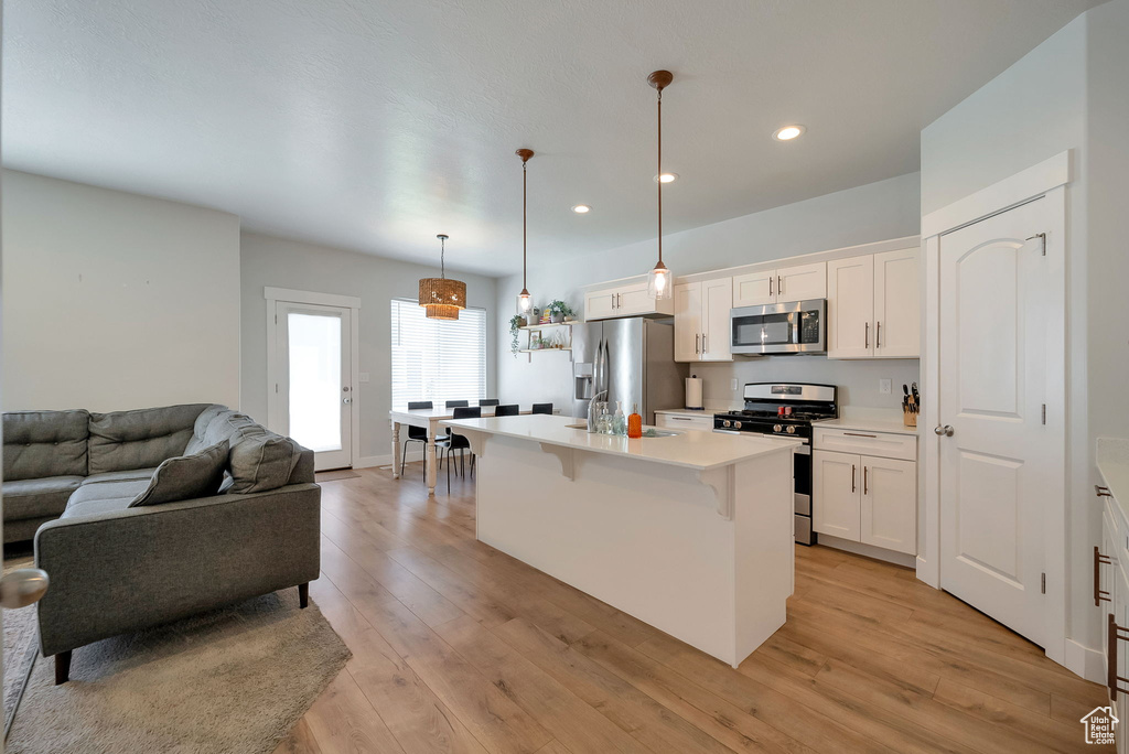 Kitchen with appliances with stainless steel finishes, open floor plan, white cabinets, recessed lighting, and a kitchen breakfast bar
