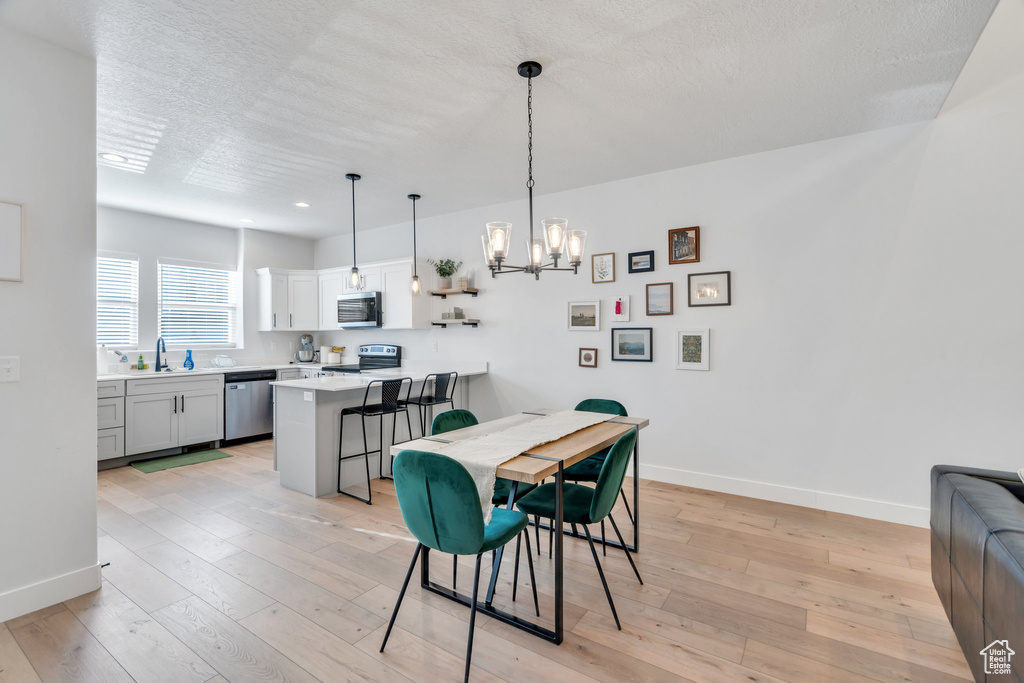 Dining room with a chandelier, light wood-style floors, a textured ceiling, and recessed lighting