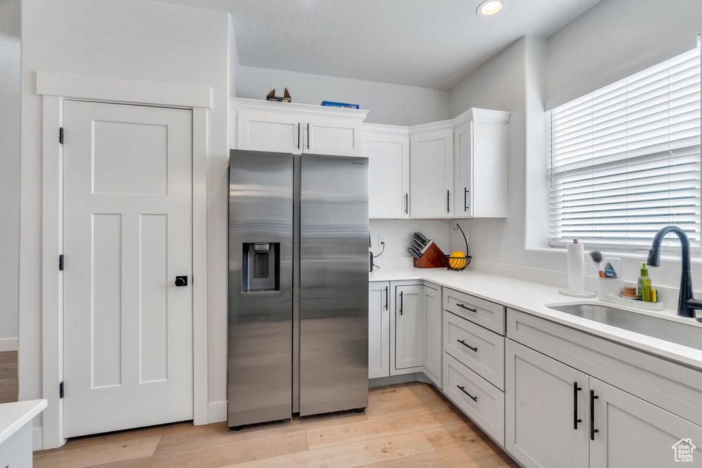Kitchen with stainless steel refrigerator with ice dispenser, light countertops, white cabinetry, light wood-type flooring, and recessed lighting