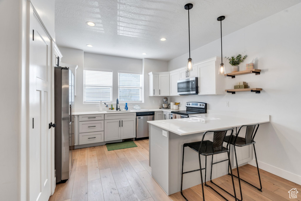 Kitchen with appliances with stainless steel finishes, a peninsula, a kitchen breakfast bar, light wood finished floors, and hanging light fixtures