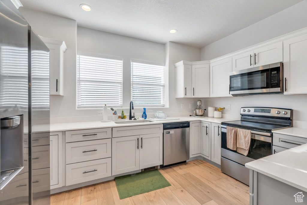 Kitchen featuring appliances with stainless steel finishes, light countertops, white cabinetry, light wood-style floors, and recessed lighting