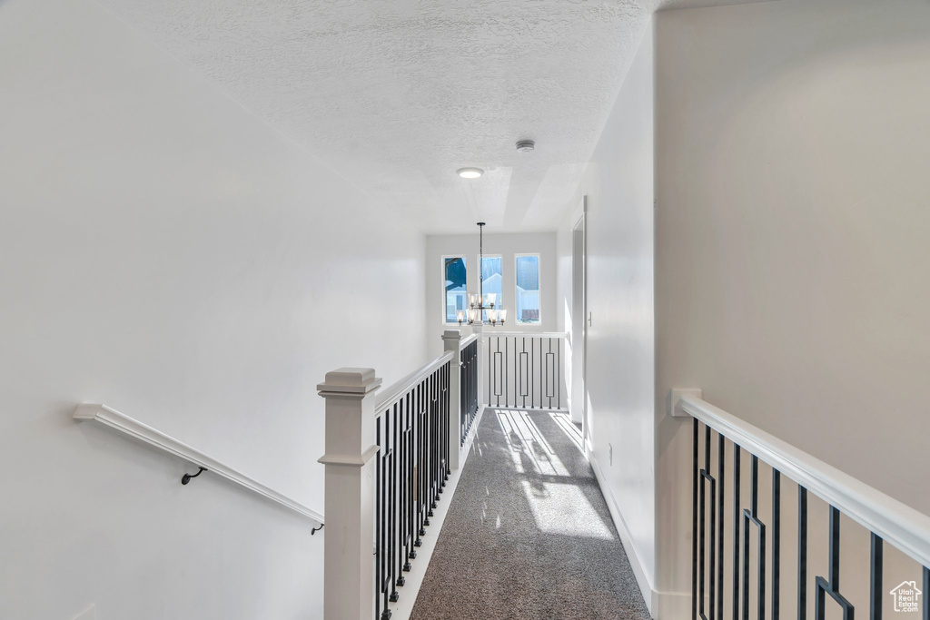Hallway featuring an upstairs landing, carpet floors, a textured ceiling, and a chandelier
