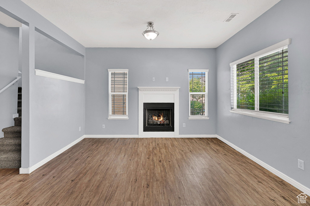 Unfurnished living room featuring stairway, wood finished floors, and a warm lit fireplace