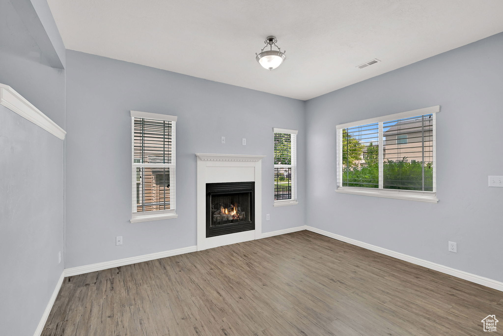 Unfurnished living room featuring wood finished floors and a lit fireplace
