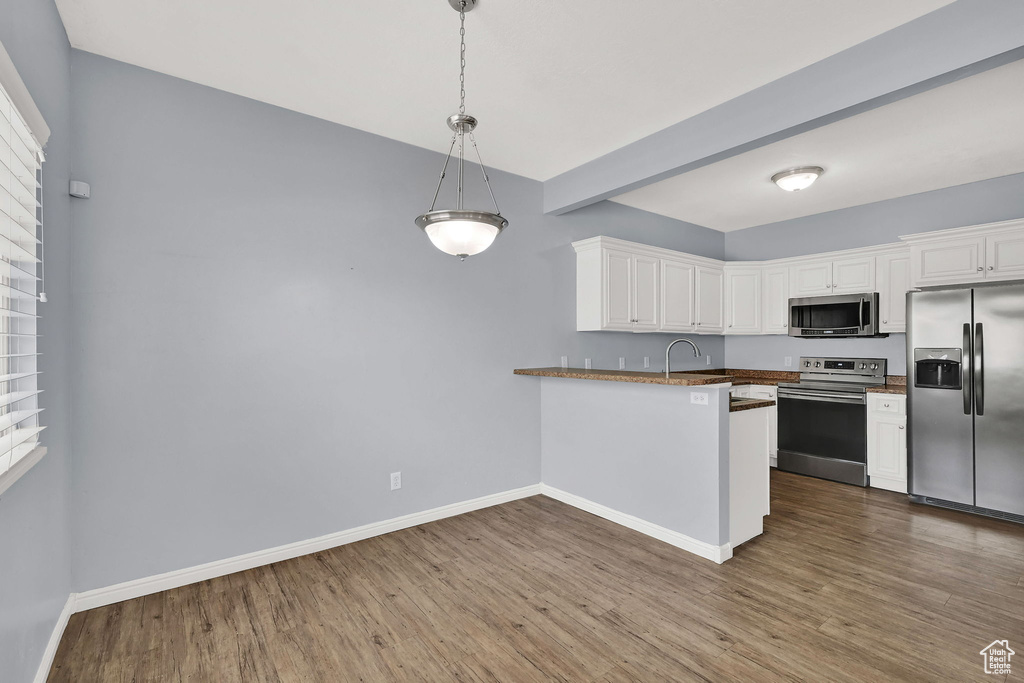 Kitchen with stainless steel appliances, white cabinetry, dark wood-style flooring, and a peninsula