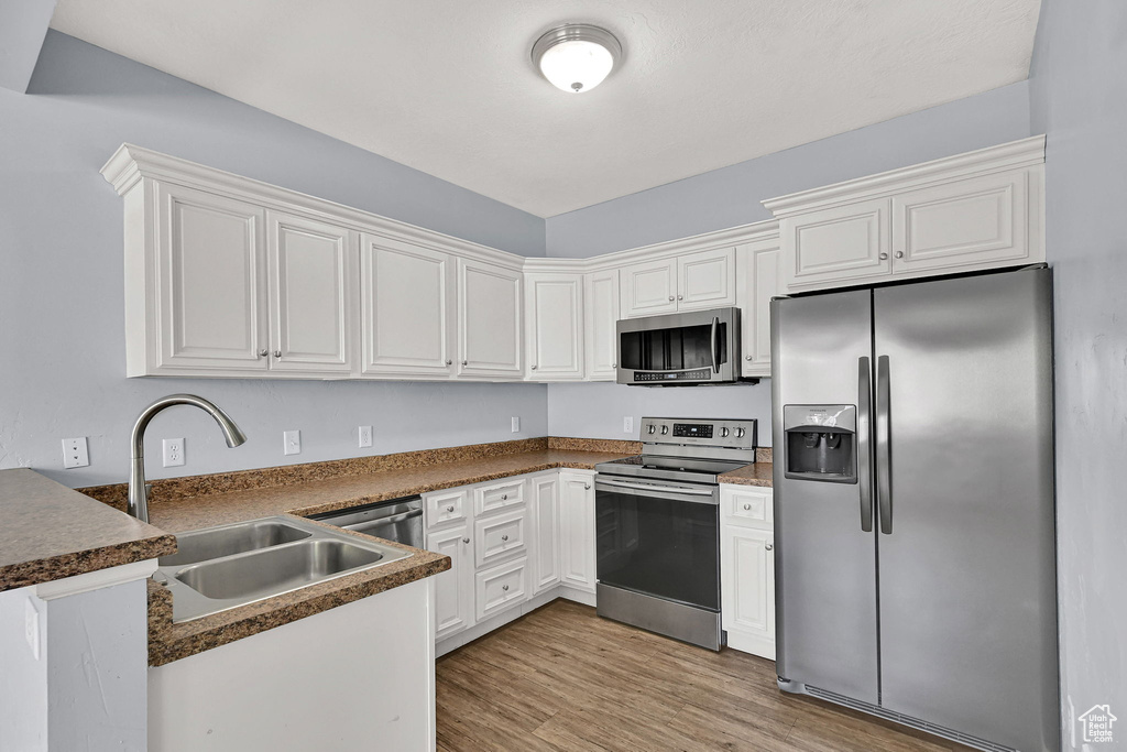 Kitchen with appliances with stainless steel finishes, a peninsula, light wood-style floors, white cabinetry, and dark countertops