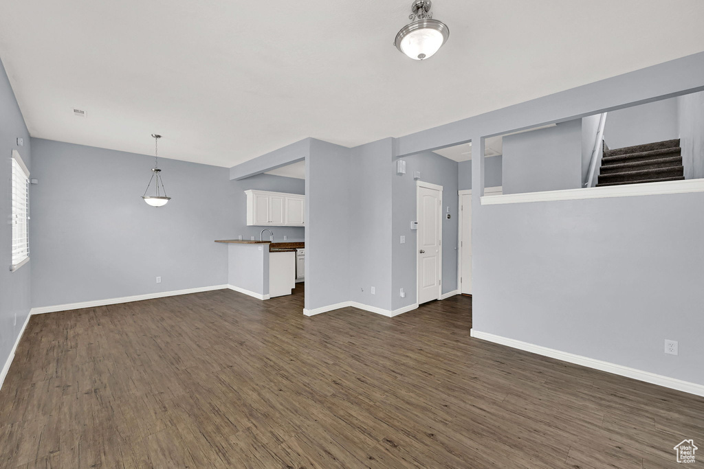 Unfurnished living room featuring dark wood-style floors and stairs