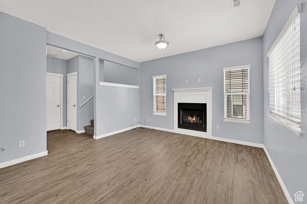 Unfurnished living room with wood finished floors, a lit fireplace, and stairway