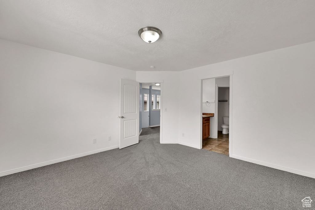 Unfurnished bedroom with dark carpet, a textured ceiling, and ensuite bathroom