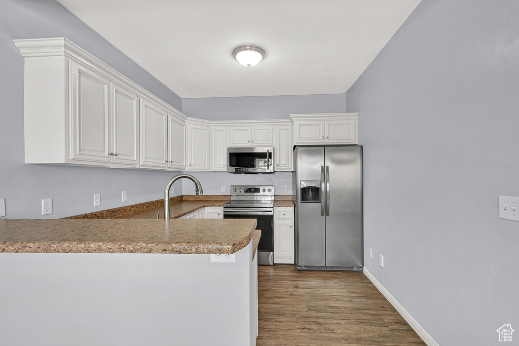 Kitchen with appliances with stainless steel finishes, a peninsula, dark wood-type flooring, and white cabinets