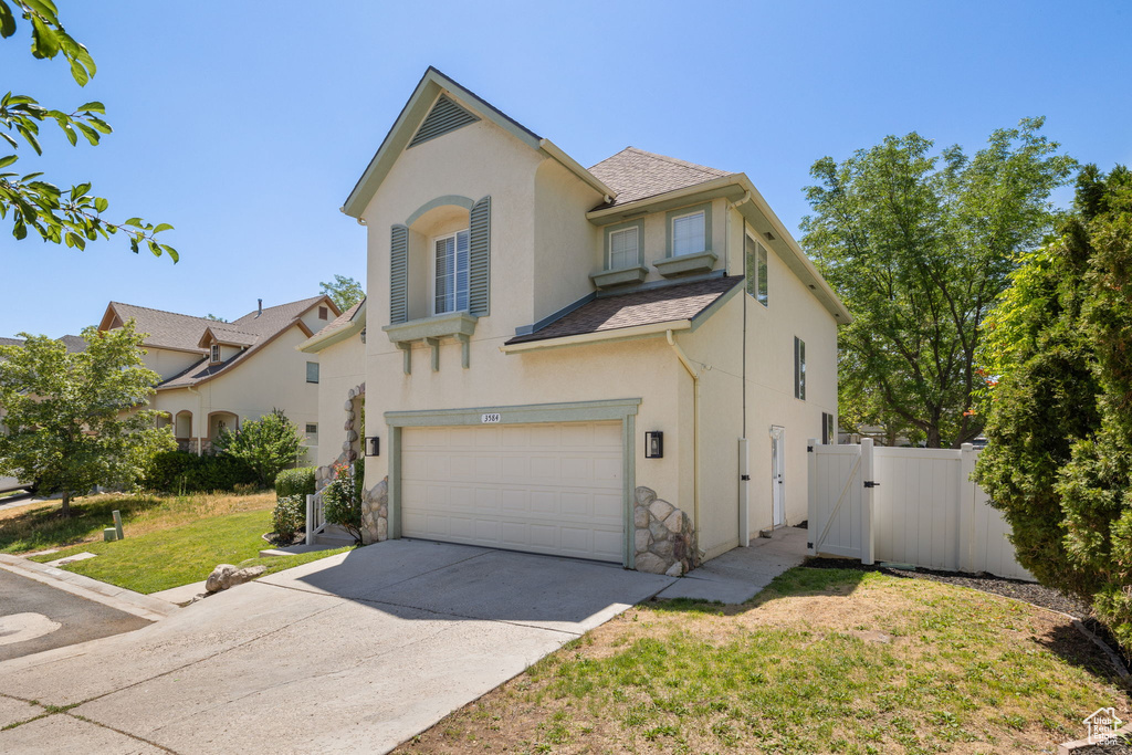View of front facade with a garage, stucco siding, driveway, a gate, and stone siding