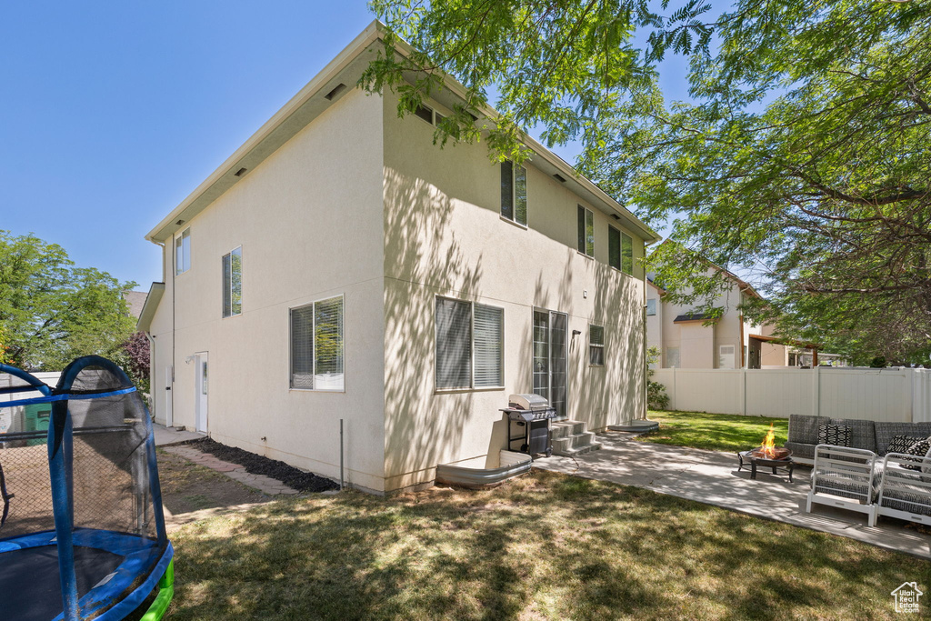 Rear view of property with a trampoline, a patio, stucco siding, and an outdoor living space with a fire pit