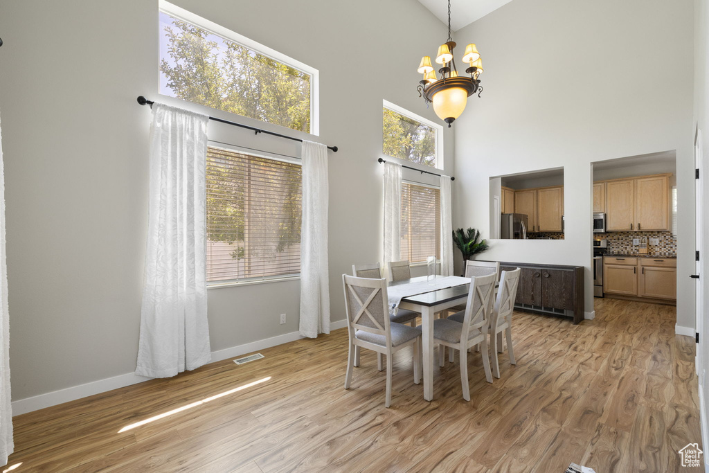 Dining room featuring a chandelier, a high ceiling, light wood-type flooring, and plenty of natural light