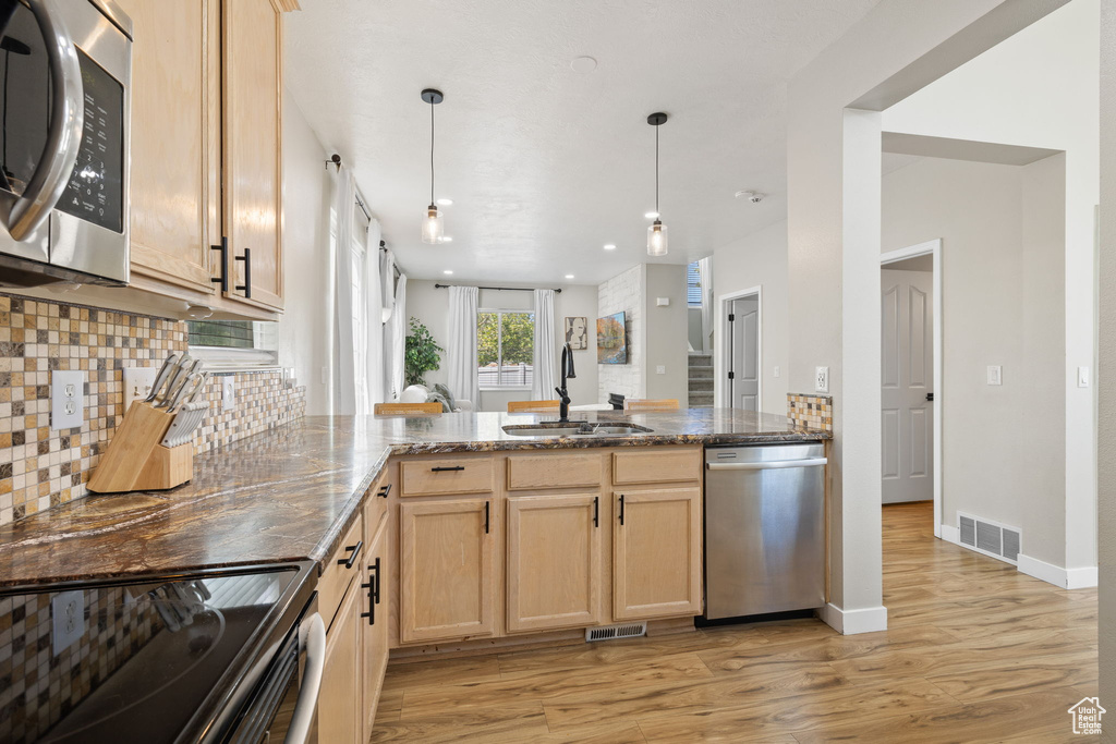 Kitchen featuring stainless steel appliances, a peninsula, light brown cabinetry, light wood-style floors, and dark stone counters
