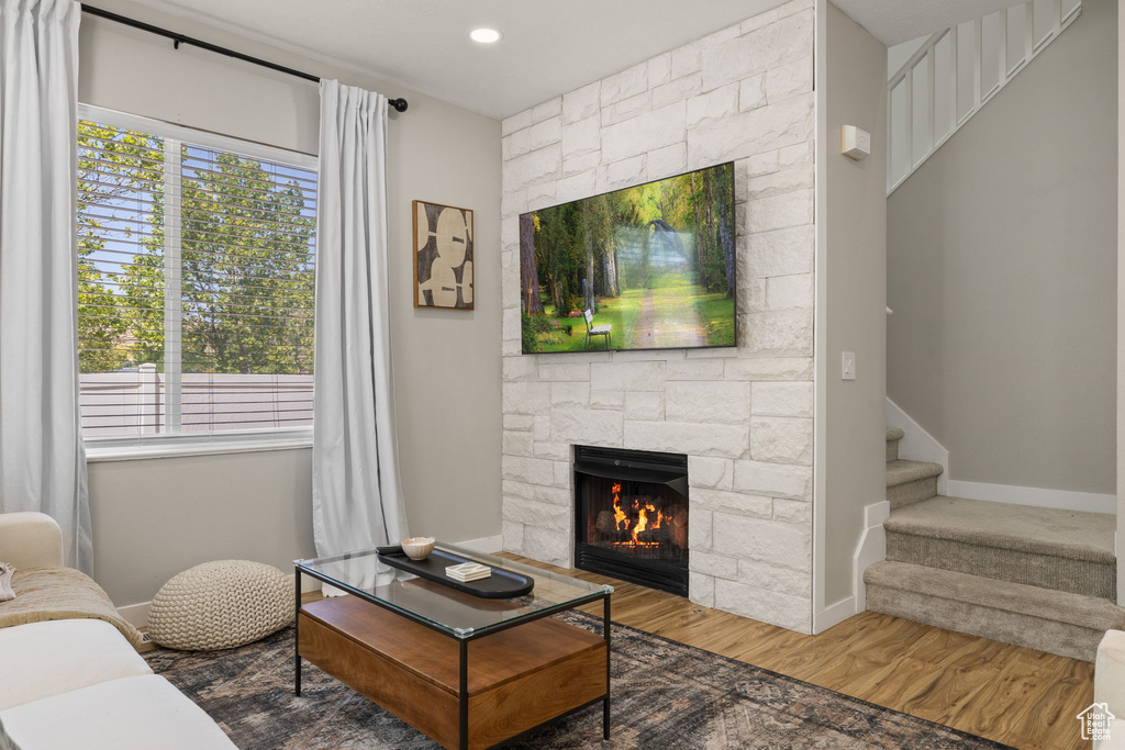 Living room with healthy amount of natural light, a stone fireplace, wood finished floors, stairs, and recessed lighting