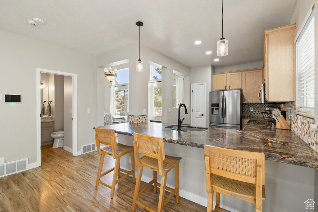 Kitchen featuring appliances with stainless steel finishes, a peninsula, light wood-style floors, backsplash, and hanging light fixtures