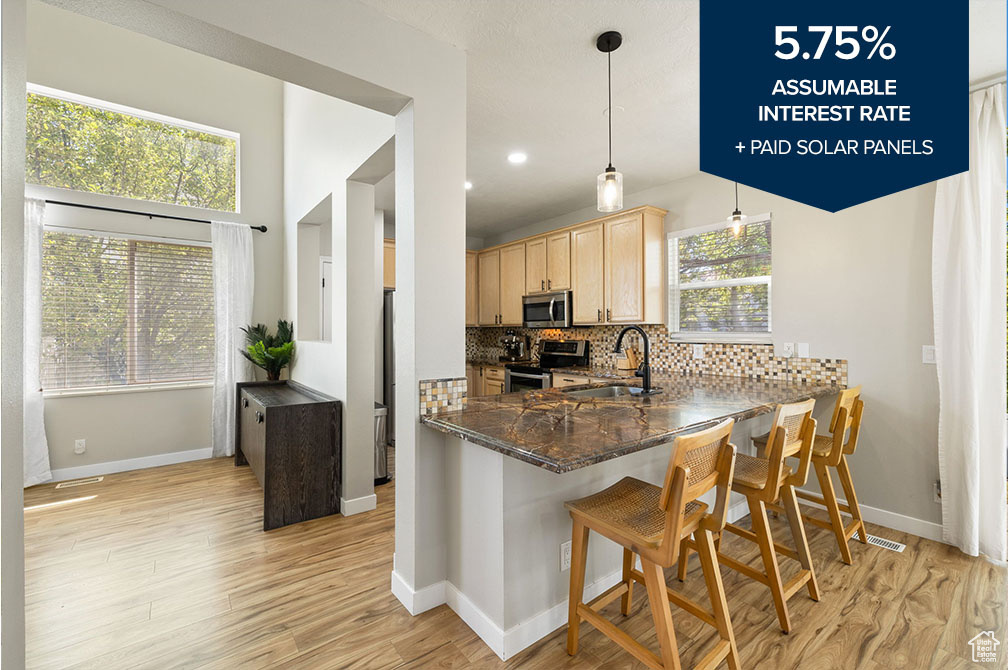 Kitchen with stainless steel appliances, light brown cabinets, backsplash, light wood-type flooring, and a breakfast bar